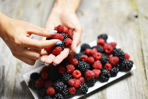 Woman picking mixed fresh berries from white plate with blackberries and raspberries

