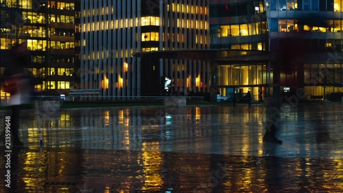 Time lapse of crowd of people walking near modern buildings in Paris business district La Defense. Night city lights, illuminated windows of office center. Concept of big city, business, job, economy