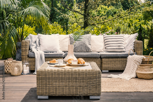 Rattan table and pillows on couch on patio in the garden during summer. Real photo