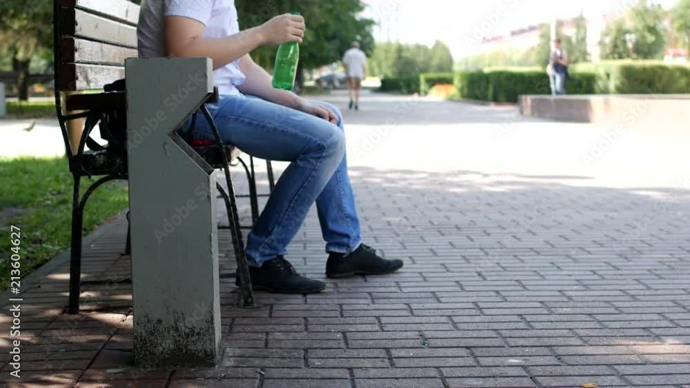 A man in the center of the city sits on a bench, drains the water and throws a plastic bottle past the trash, litter A man in the center of the city sits on a bench, drains the water and throws a plastic bottle past the trash, litter