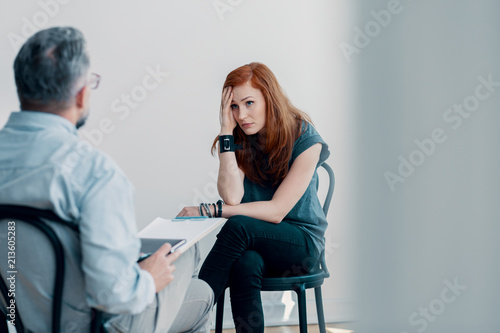 Scared young woman talking to a therapist about abuse in a bright office