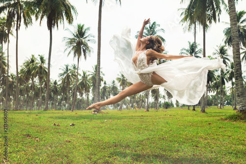 Beautiful bride is jumping in dance  on the field with a lot of palm trees