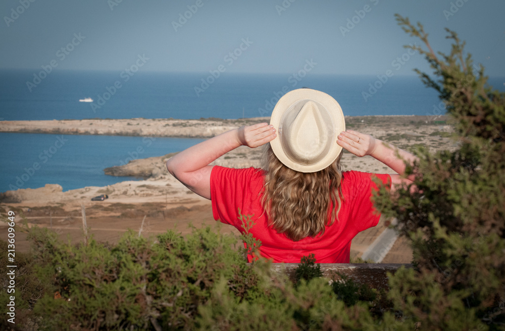 A girl in a hat looks at the sea. Cape Cave Greco, Cyprus, 2018