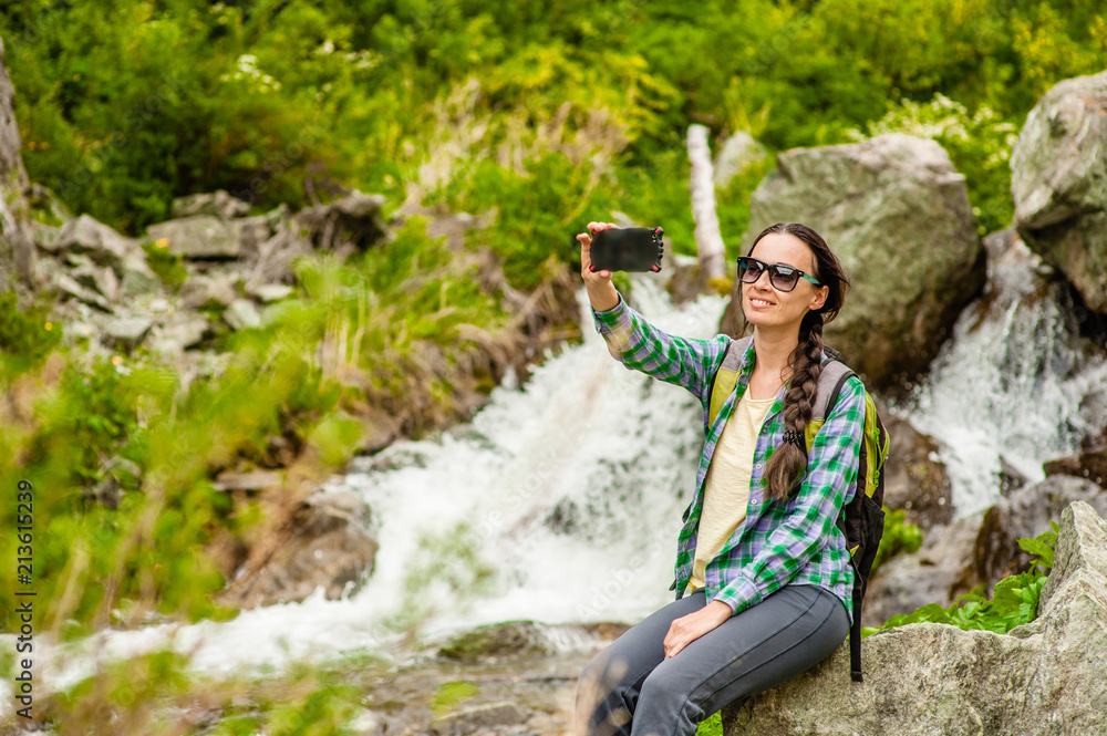 Naklejka premium woman hiker taking selfie with smartphone near a waterfall