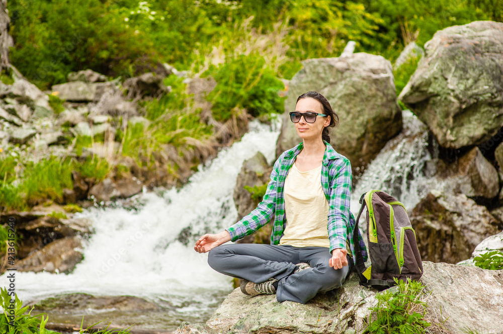 young woman doing lotus position yoga near waterfall