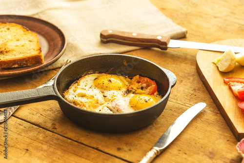 Rye scrambled eggs with onions and tomatoes in a frying pan on a rustic wooden background