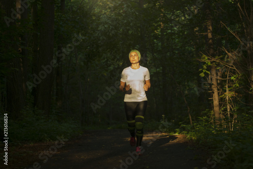 girl is beautifully illuminated by the sun rays while jogging in the dark evening or morning forest