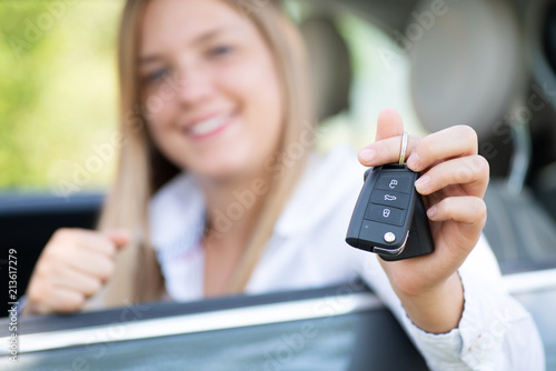 Junge Frau freut sich über ihr Auto und hält die Autoschlüssel in der Hand 