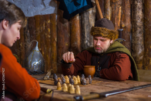 Two men in russian ethnic suit playing medieval popular strategy board game - tafl. Folk, competition and traditional concept photo