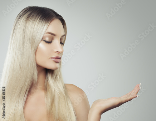 Beautiful Young Woman with Clean Fresh Skin and Blonde Hair Showing Empty Copy Space on the Open Hand. Product Placement and Advertising Marketing Concept