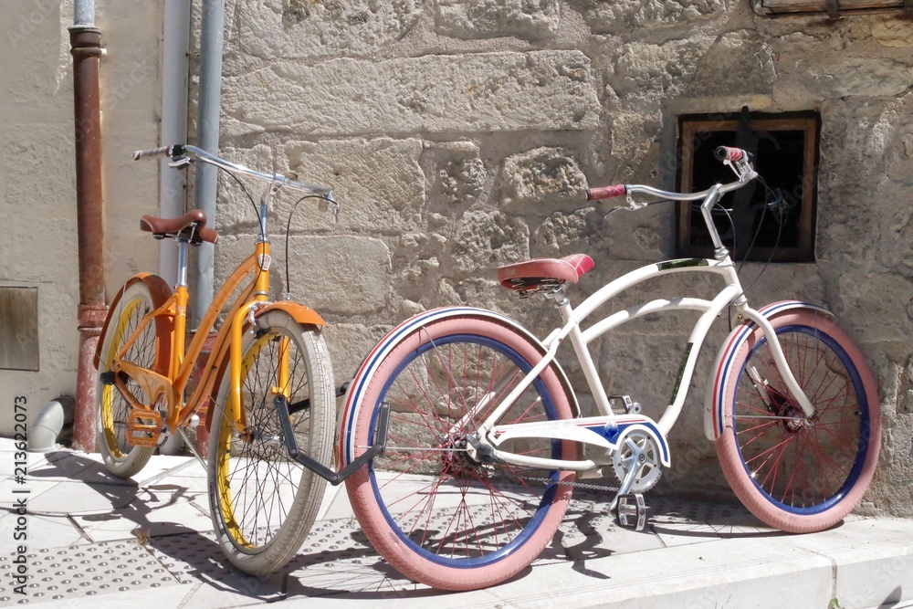 Two retro bicycles parked against a stone wall in a medieval village. This mean of transport became a symbol for the ecologists.