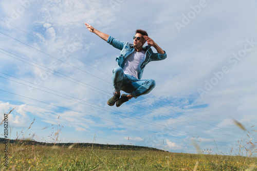young man with sunglasses salutes whle jumping outside