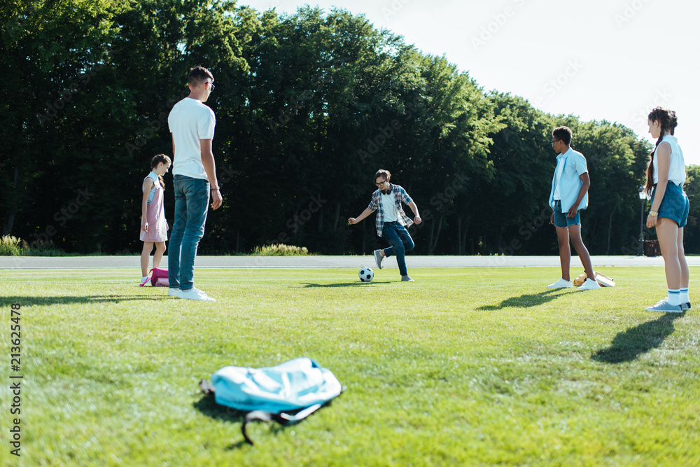 Obraz premium multiethnic teenage classmates playing with soccer ball in park