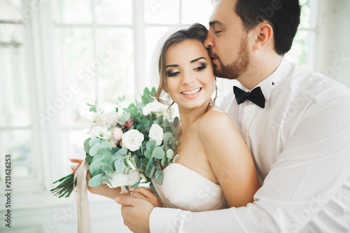 Gorgeous groom gently hugging stylish bride. Sensual moment of luxury wedding couple