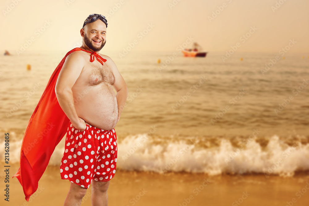 Funny fat man in a superhero costume on the beach by the sea on vacation in  the summer. Stock Photo | Adobe Stock
