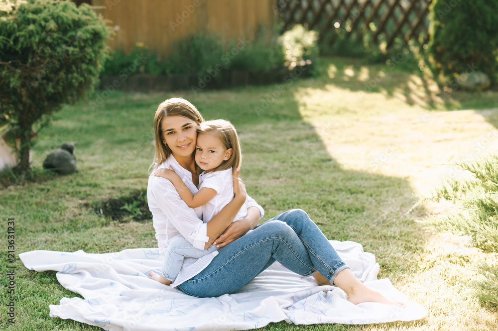 Fototapeta premium happy mother and little daughter hugging each other while resting on cloth together on backyard