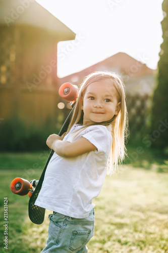 portrait of smiling adorable little skater with penny board in hands on yard