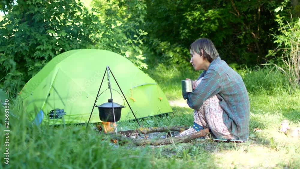 Independent young traveler woman hiker, keeping warm and relaxing by campfire Independent young traveler woman hiker, keeping warm and relaxing by campfire