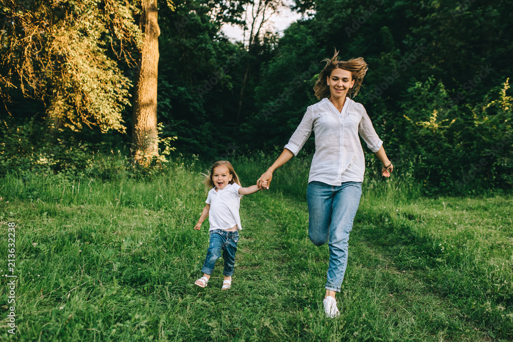 Fototapeta premium young mother and cheerful daughter holding hands while running together in forest