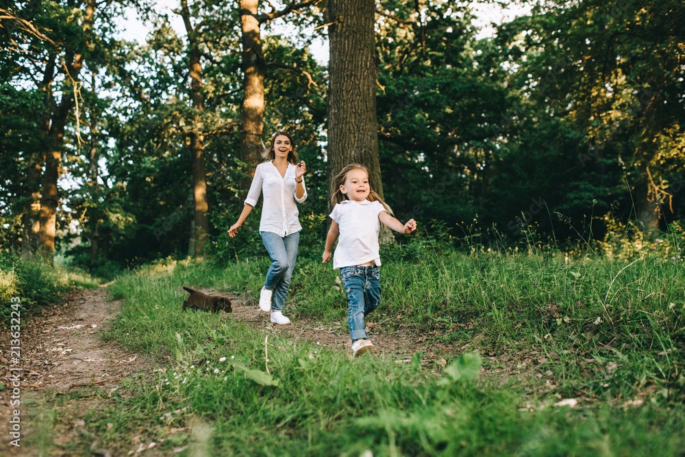 mother and smiling daughter with labrador puppy running together in forest mother and smiling daughter with labrador puppy running together in forest