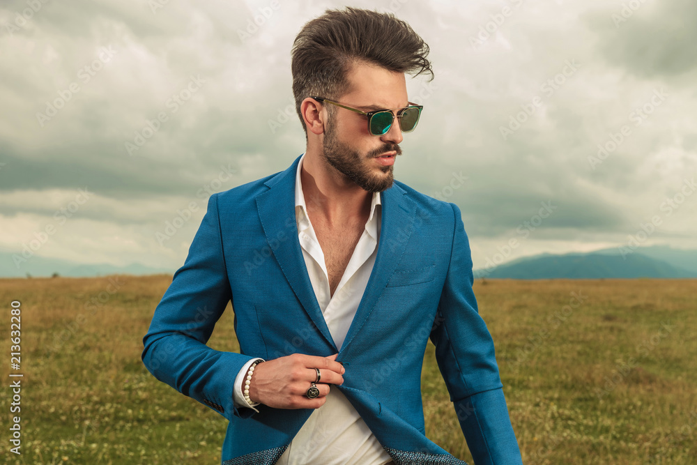 attractive smart casual man with sunglasses buttoning blue suit outside ...