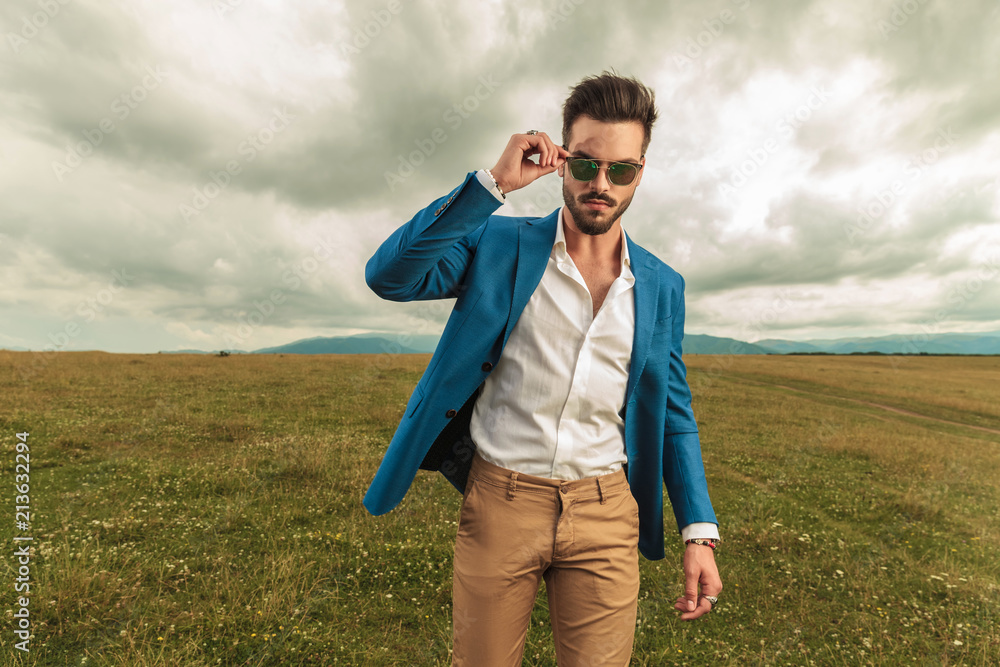attractive man in suit arranges his sunglasses while standing outside attractive man in suit arranges his sunglasses while standing outside