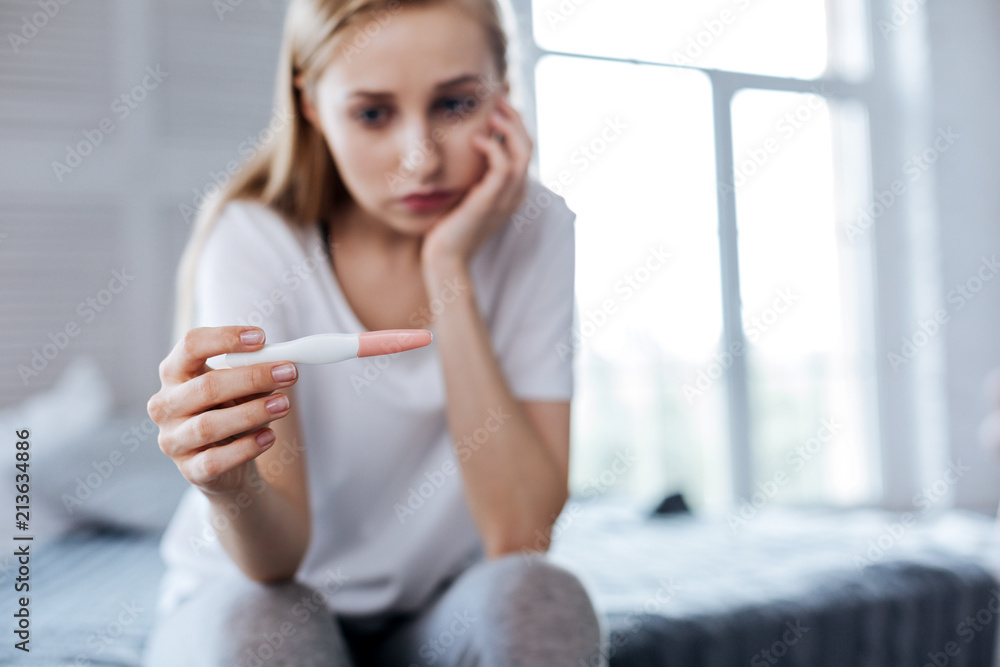 Unexpected result. Unhappy pretty woman sitting and holding her pregnancy test Unexpected result. Unhappy pretty woman sitting and holding her pregnancy test
