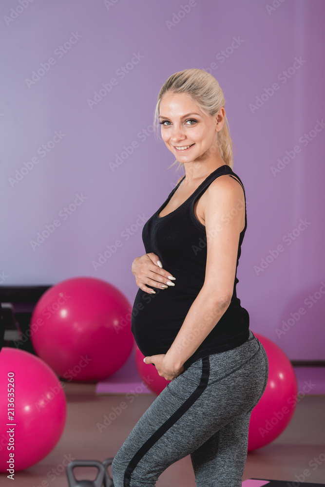 Pregnant woman stand in the gym, holding her belly on 9 month with lovely eyesight Pregnant woman stand in the gym, holding her belly on 9 month with lovely eyesight