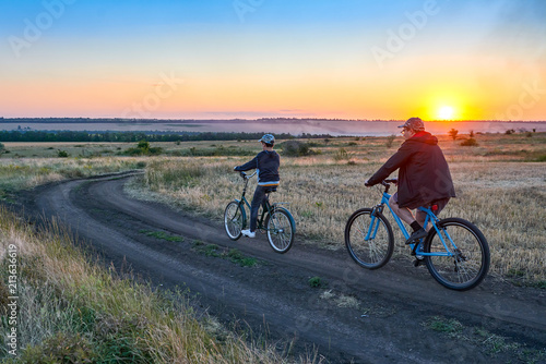 father and son ride a bike in the country on the field in the evening