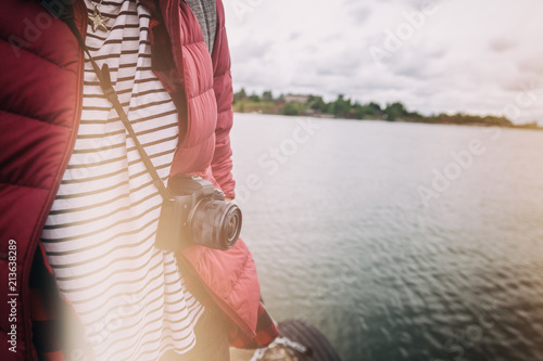 A camera on a strap on a man on a background of a landscape with water, an image with a retro toning. Travel, blogging, reporting, art and creativity concept