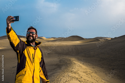 man traveler take a selfie picture using the smartphone with a desert and ocean in background. adventure and alternative vacation concept for caucasian people. enjoy life and freedom and nature