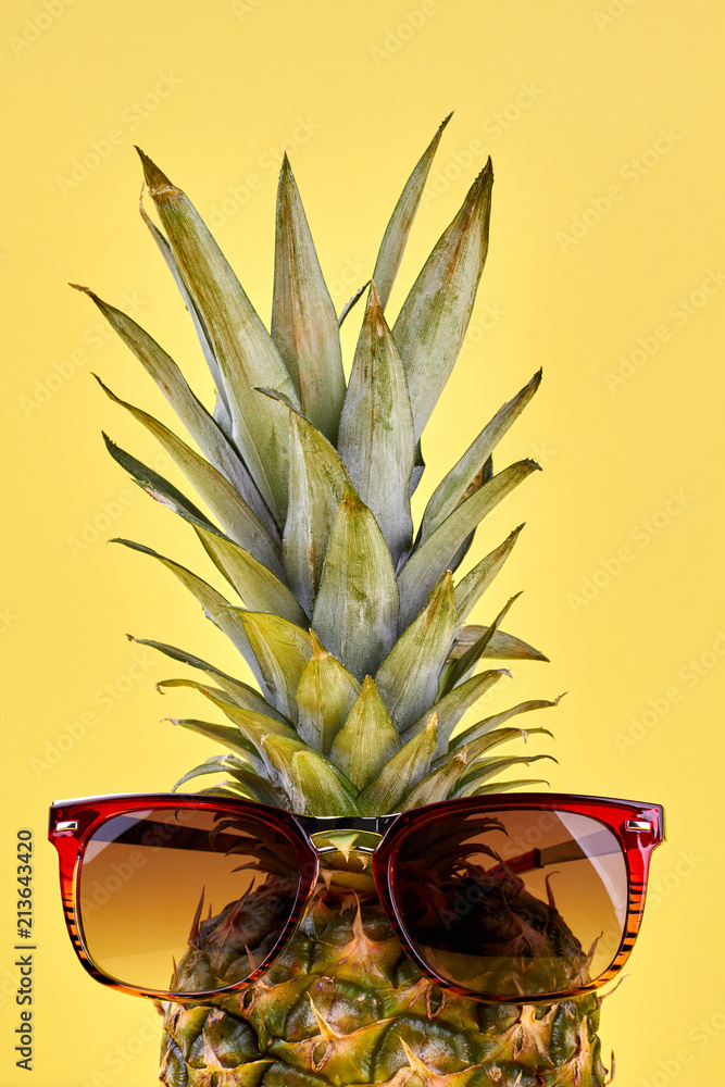 Organic pineapple wearing sunglasses. Fresh exotic pineapple in sunglasses on color background. Summer and rest concept.