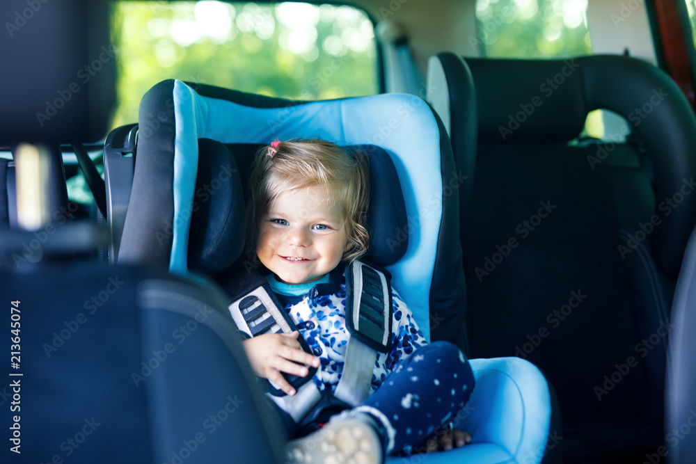 Adorable baby girl with blue eyes sitting in car safety seat. Toddler child going on family vacations and jorney. Adorable baby girl with blue eyes sitting in car safety seat. Toddler child going on family vacations and jorney.