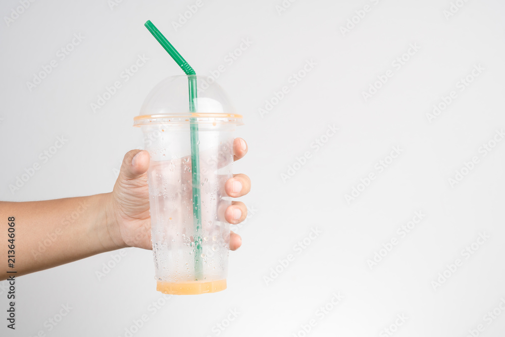 Hand holding empty plastic cup of Thai milk ice tea with green straw Hand holding empty plastic cup of Thai milk ice tea with green straw