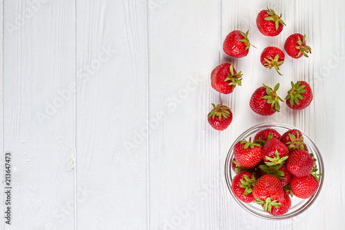 Fototapeta Naklejka Na Ścianę i Meble -  Ripe fragrant strawberries and copy space. Sweet healthy strawberries in glass bowl on white wooden background, top view.