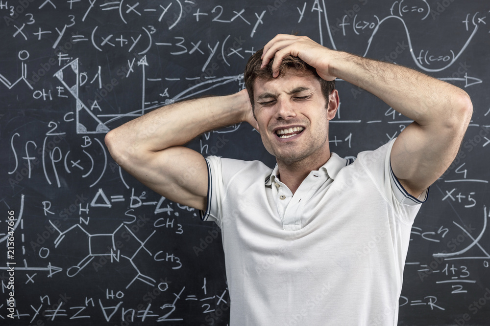  portrait of a student near the blackboard holding his arms to his head in a sign of stress and disappointment. concept of study and learning difficulties.