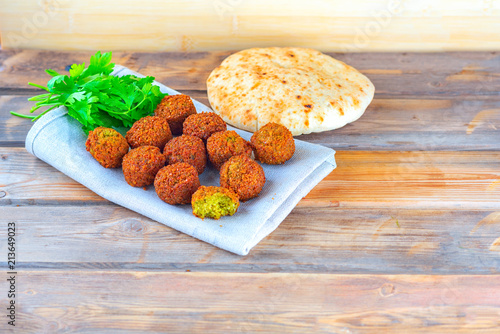 Falafel balls, pita and green fresh parsley on a wooden background, rustic style. Falafel is a traditional Middle Eastern food, commonly served in a pita.