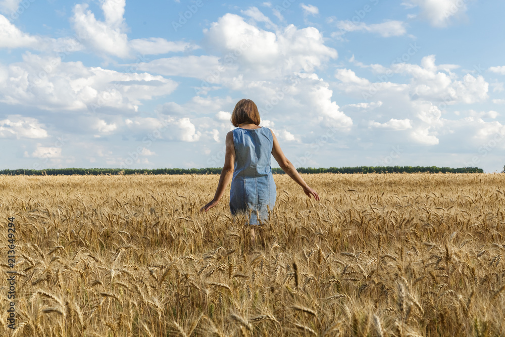 The girl is on the yellow wheat field. White clouds and blue sky in the background.