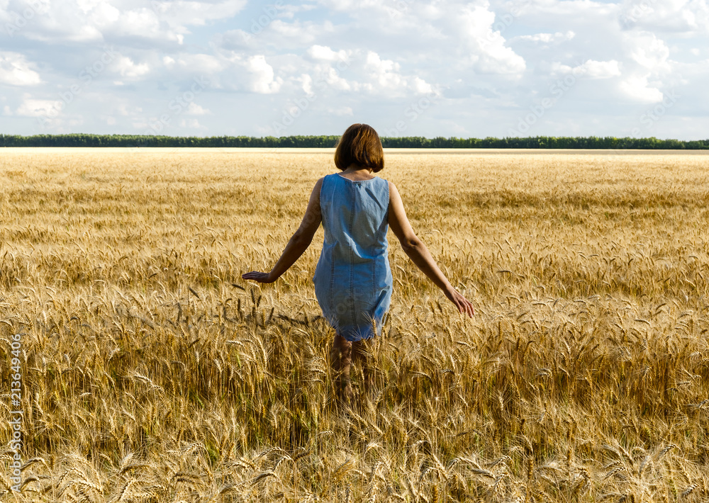 The girl is on the yellow wheat field. White clouds and blue sky in the background. The girl is on the yellow wheat field. White clouds and blue sky in the background.