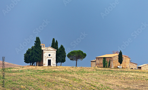 Italy. Tuscany. Val d'Orcia. Pienza. Famous old Cappella della Madonna di Vitaleta 1590 and cypress trees on the hill against the background of the autumn blue sky photo