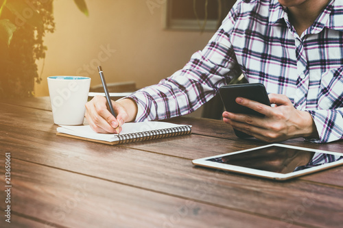 asia woman writing and holding phone on wood table in coffee shop. Vintage toned.