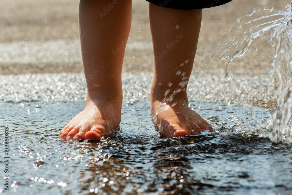 Kleinkind planscht mit nackten Füßen in spritzender Wasserpfütze Kleinkind planscht mit nackten Füßen in spritzender Wasserpfütze