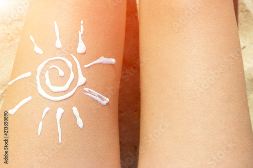 Woman sunbathing on the beach with a drawing of sun on her leg with cream