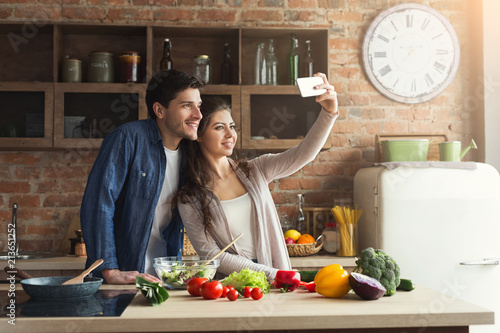 Happy couple cooking and taking selfie in kitchen
