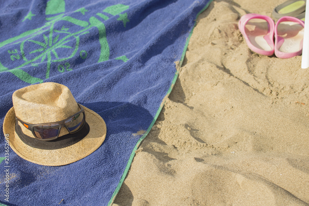 closeup of men's straw hat on blue beach towel with sand in the background closeup of men's straw hat on blue beach towel with sand in the background
