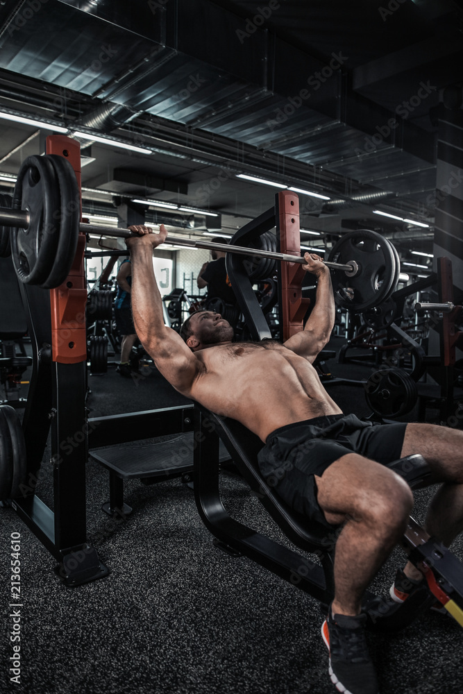 Athletic young man laid on back working his chest with heavy barbell