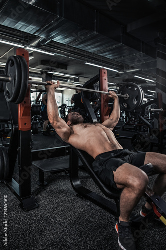 Obraz na płótnie Athletic young man laid on back working his chest with heavy barbell w salonie