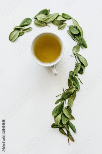 A mug of fragrant and useful herbal tea. A dried herb is lying next to it for cooking