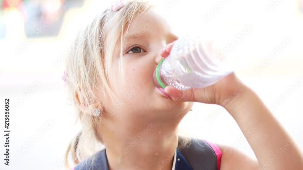 The child blond girl with pleasure drink water outdoors. A child is drinking clean water from a bottle The child blond girl with pleasure drink water outdoors. A child is drinking clean water from a bottle