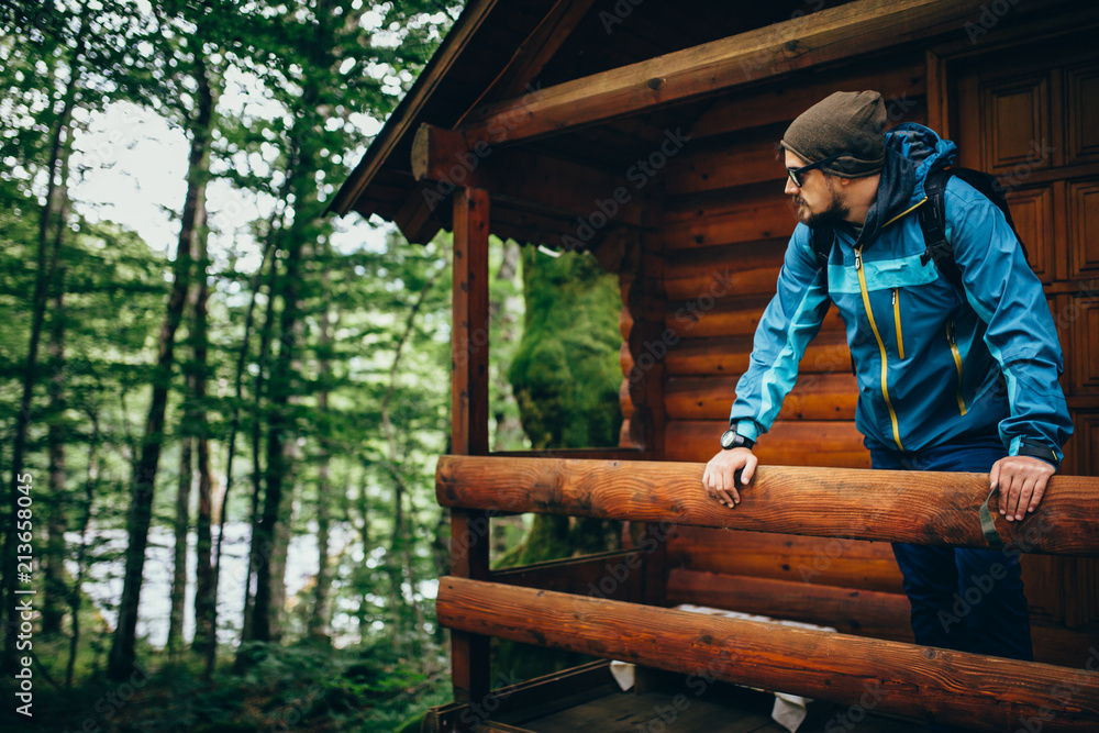 Man standing at the balcony of wooden house in forest Man standing at the balcony of wooden house in forest